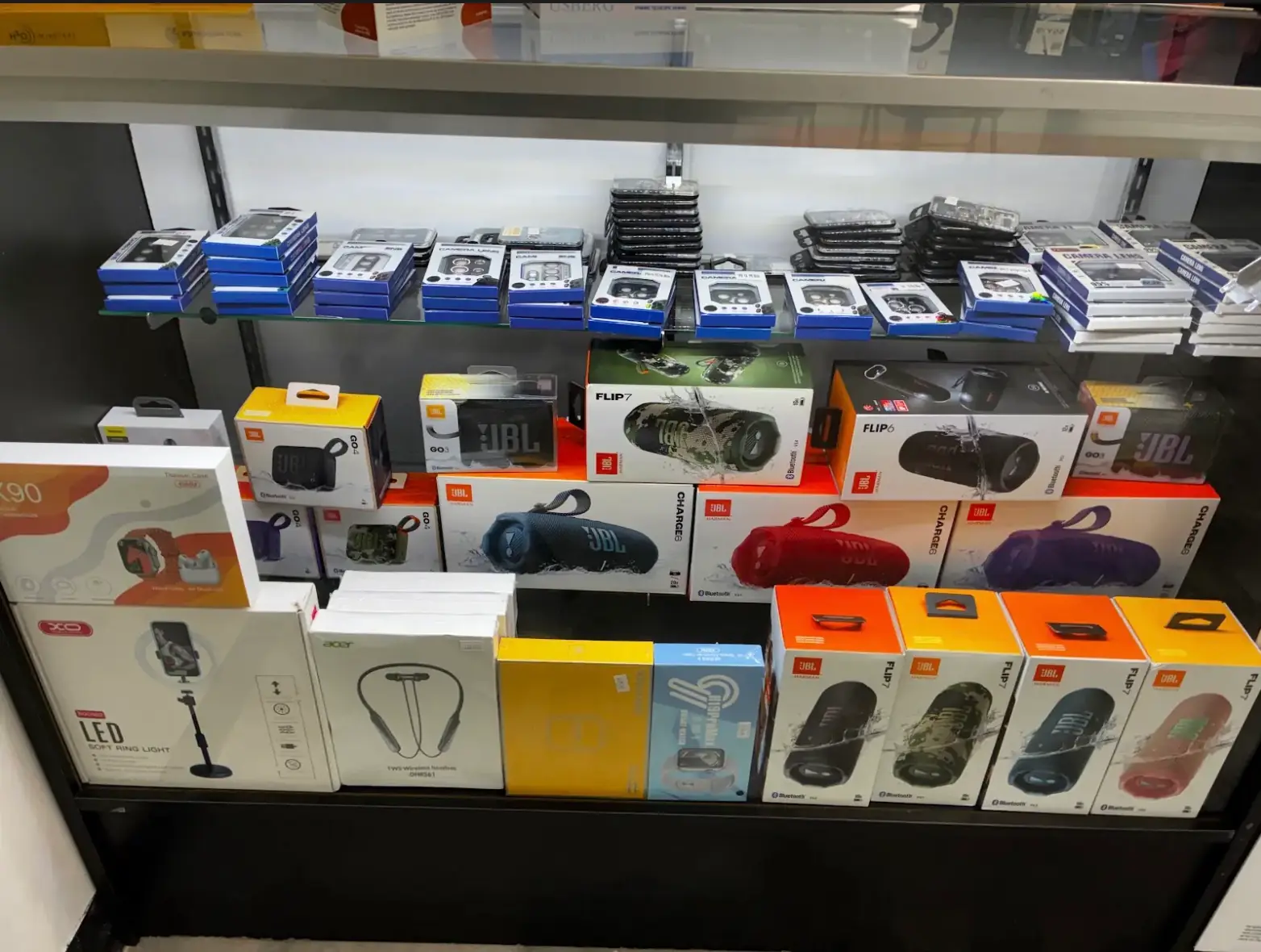 JBL Flip 7, Charge 6 and Go 4 speakers and camera lens protectors in the display case